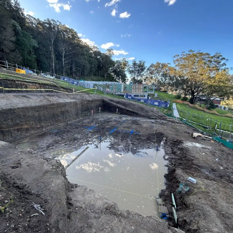 Flooded footings on a Lou Projects building site after rain, with water pooled across the excavated slab