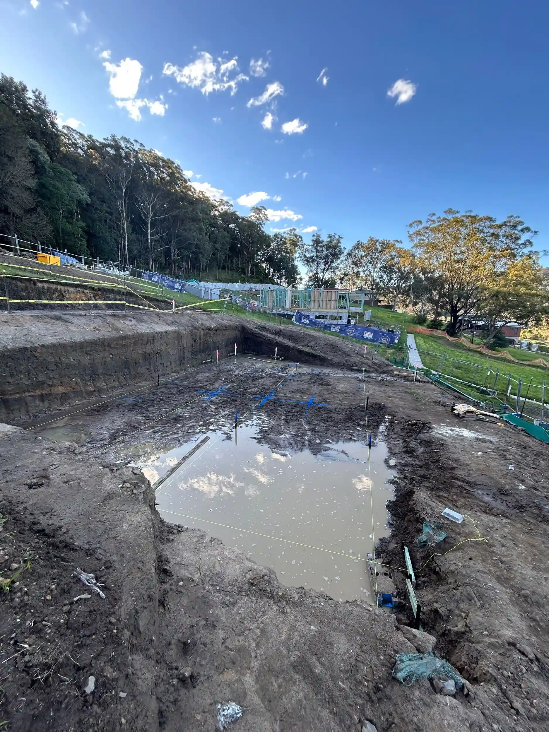 Flooded footings on a Lou Projects building site after rain, with water pooled across the excavated slab