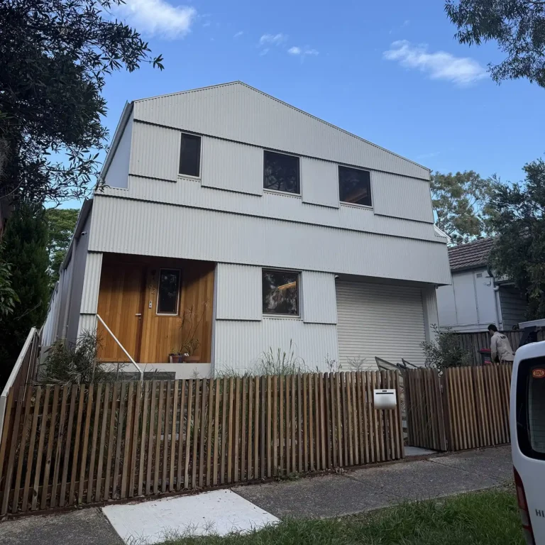 Lou Projects Hercules House - upper level of Certified Passivhaus showing off-white Colorbond corrugated cladding, three vertical windows and pitched gable form